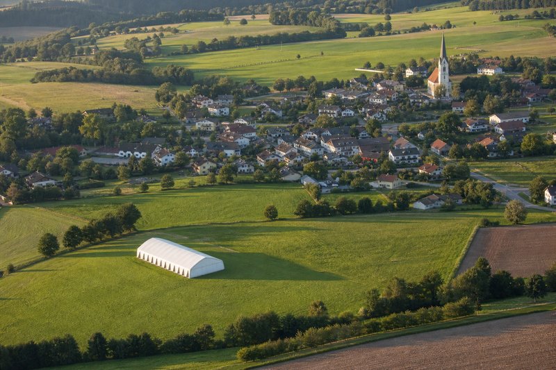 Luftaufnahme: österreichische Gemeinde mit Feldern und einem Weidezelt auf einer Wiese
